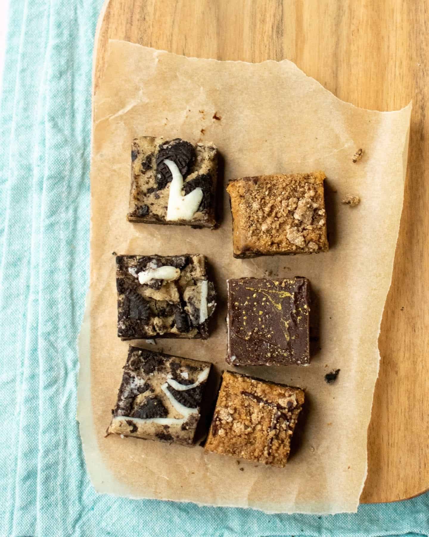 A closer photo of chocolate brownies. There are 6 in total, with 3 of them having cookie dough and oreo pieces on top, 2 have a Biscoff biscuit crumb on top and the other one has a chocolate top.