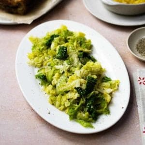 An oval plate of cooked leeks and cabbage with dishes just visible in the background