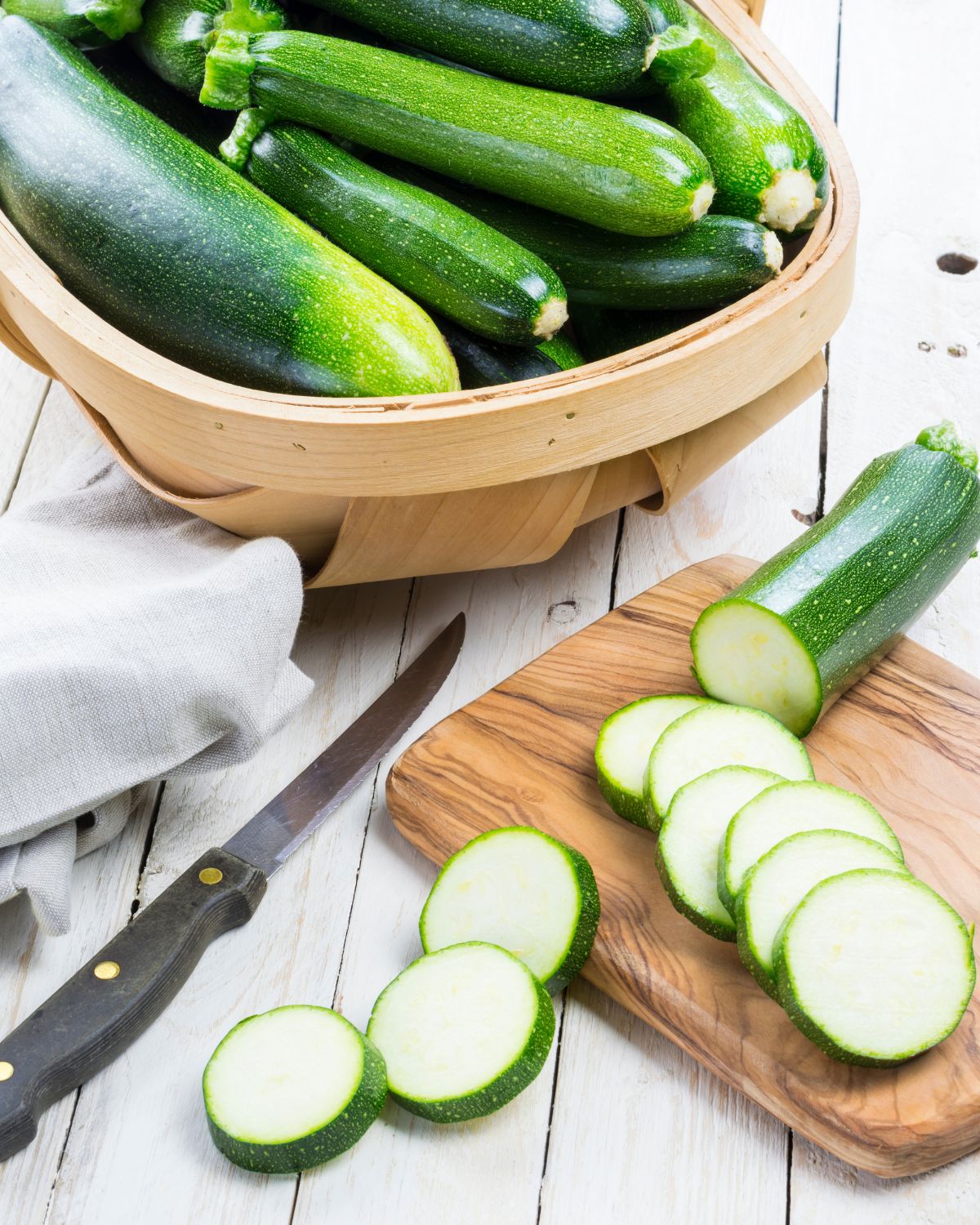 Many zucchini in a basket and chopped on a chopping board.