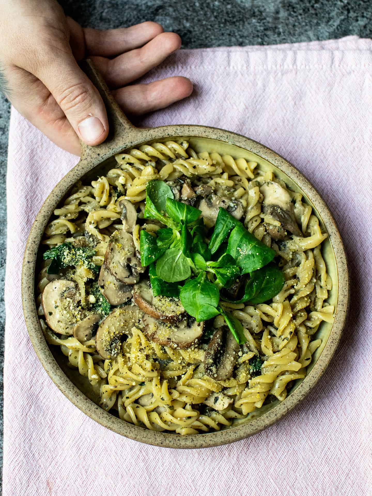 A top down photo of a bowl of creamy mushroom pasta with a hand holding the bowl.