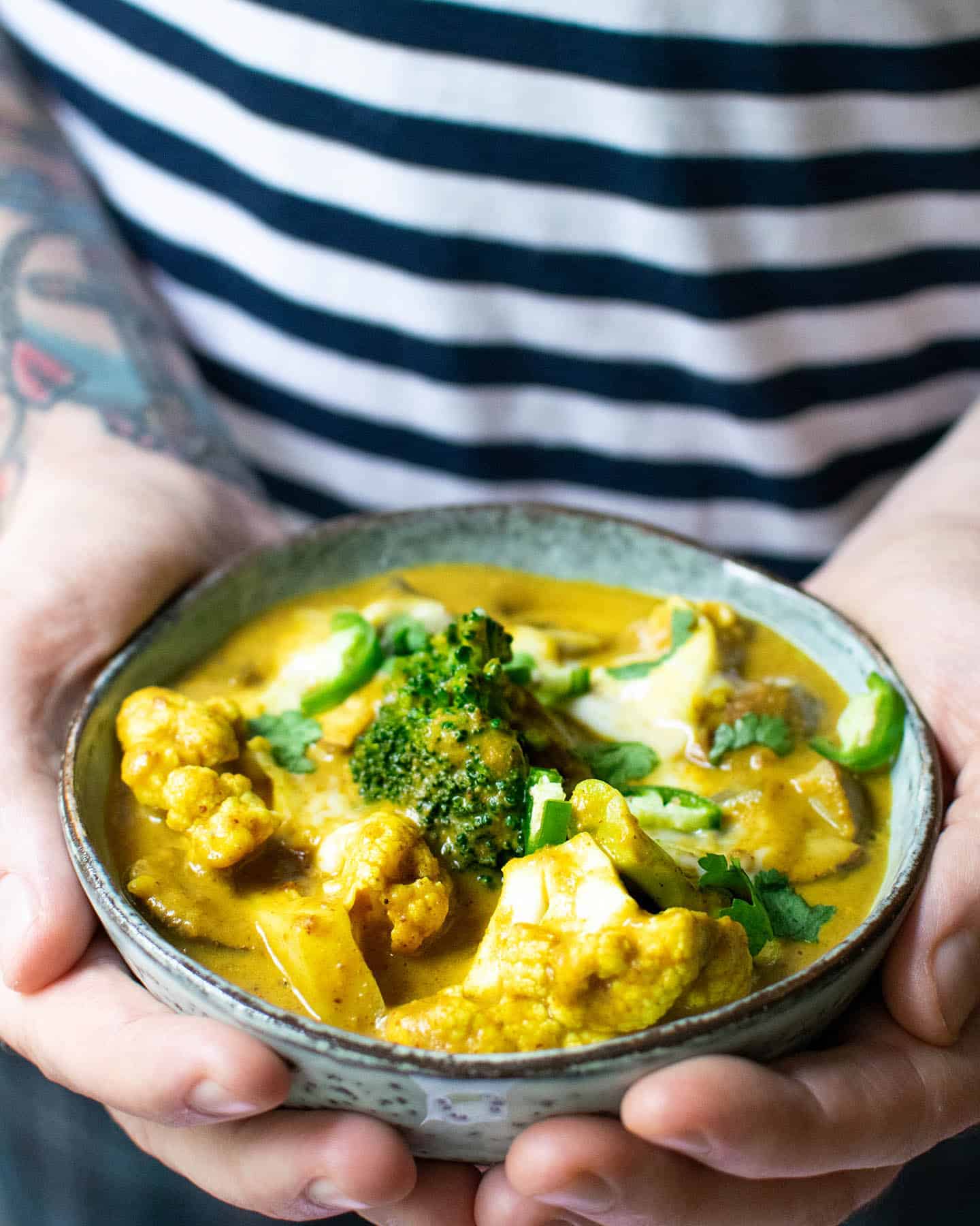 A man holding out a bowl of peanut butter curry, set against a blue and white t-shirt