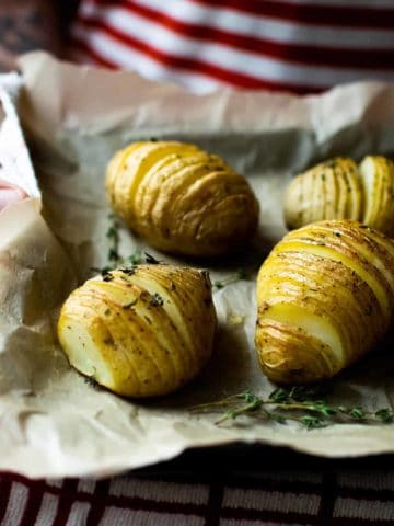 A man wearing a red and white striped t-shirt holding a baking tray of vegan hasselback potatoes, with greaseproof paper on the tray