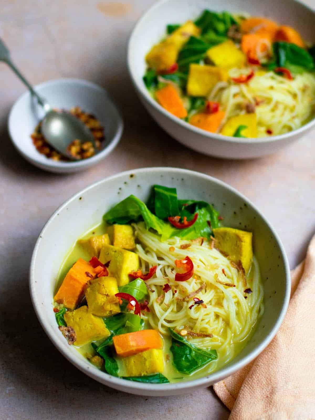 Two bowls of vegan khao soi topped with fresh chilli