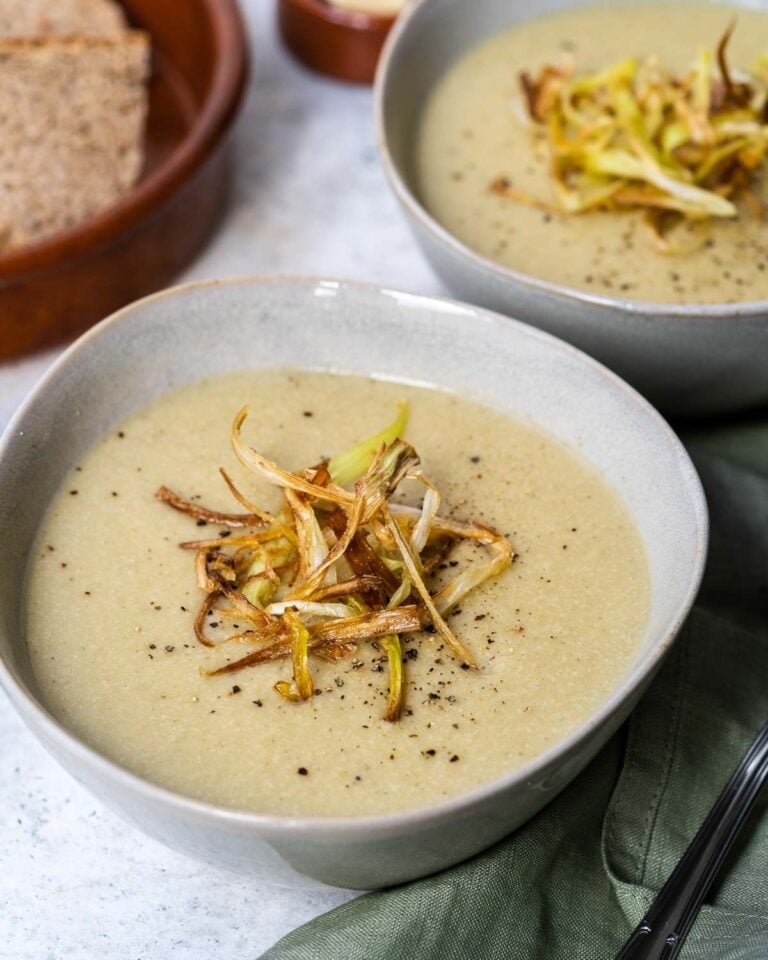 Leek and potato soup in a bowl topped with crispy leeks and served with bread.
