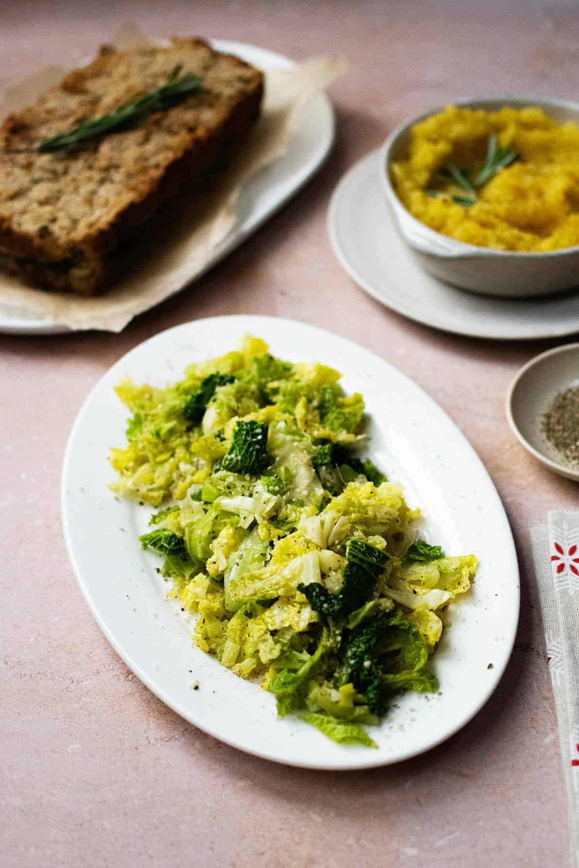 Leeks and cabbage on an oval white plate on an angle. There's nut roast and swede mash in the background