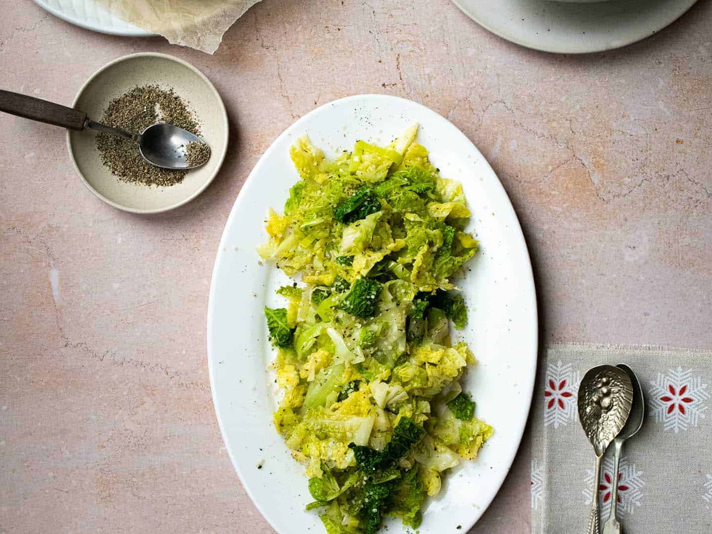 Landscape image showing cabbage and leeks on a white oval plate with spoons and black pepper in a dish