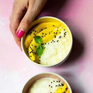 A bowl filled with mango slices and creamy, coconut-y rice, topped with black sesame seeds.