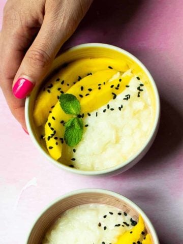 A bowl filled with mango slices and creamy, coconut-y rice, topped with black sesame seeds.