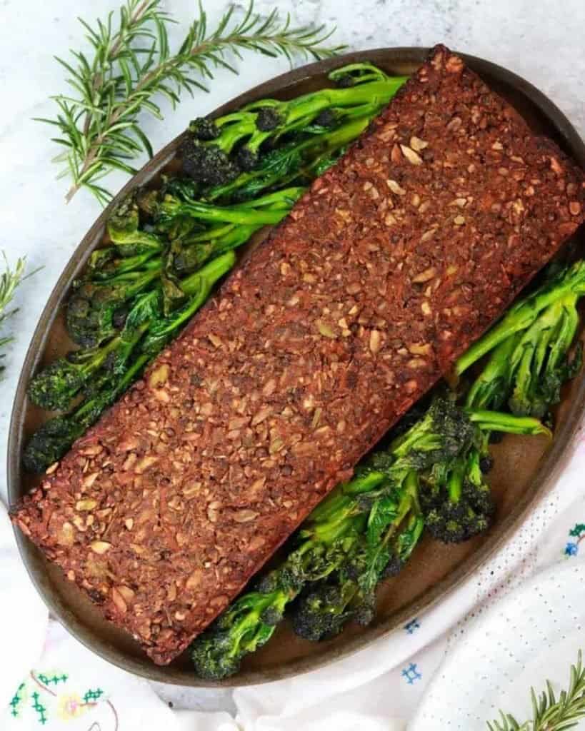 Lentil loaf on a serving plate with broccoli, and rosemary surrounding it