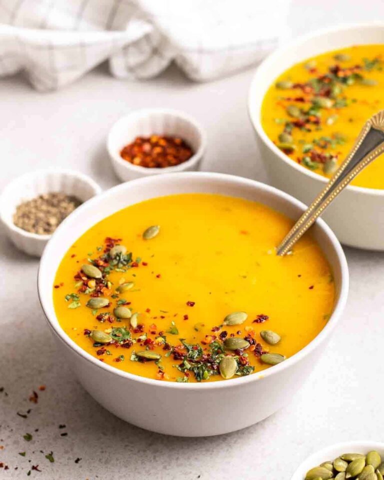 Creamy pumpkin potato soup in two bowls topped with chili flakes and pumpkin seeds.