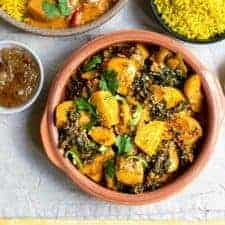 Saag Aloo just off centre to the right with chutney in a small bowl to the left, spoons to the right and rice and curry above it.