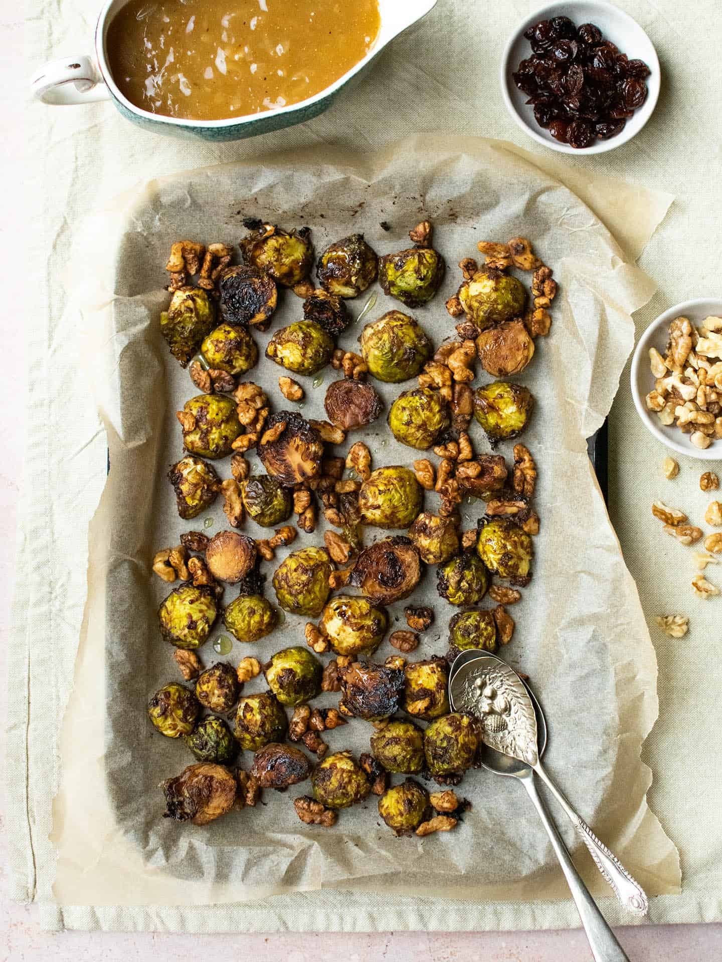 A parchment lined tray of vegan roasted Brussels sprouts, sprinkled with walnuts.