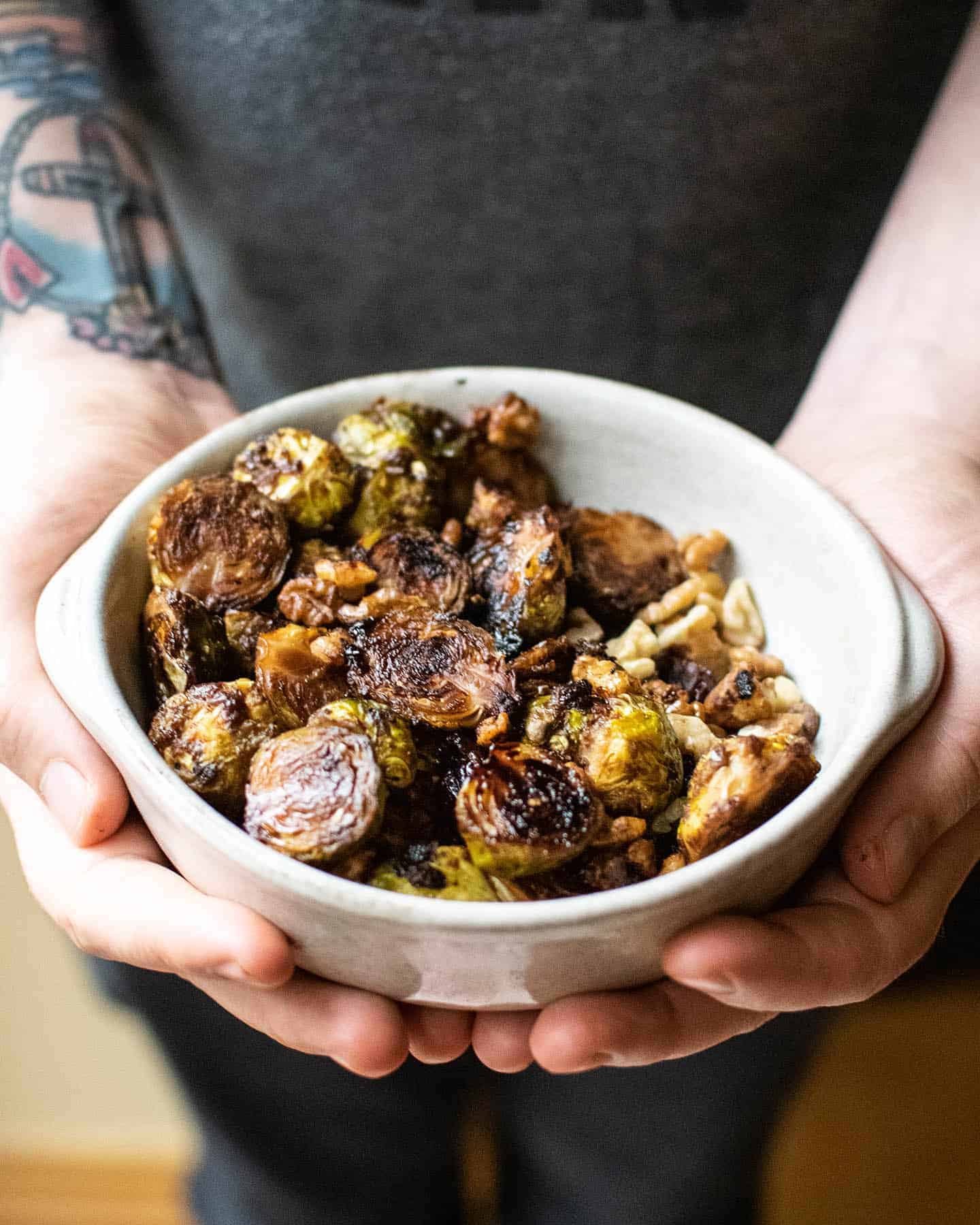 A small bowl filled with roasted sprouts being held in a pair of hands.