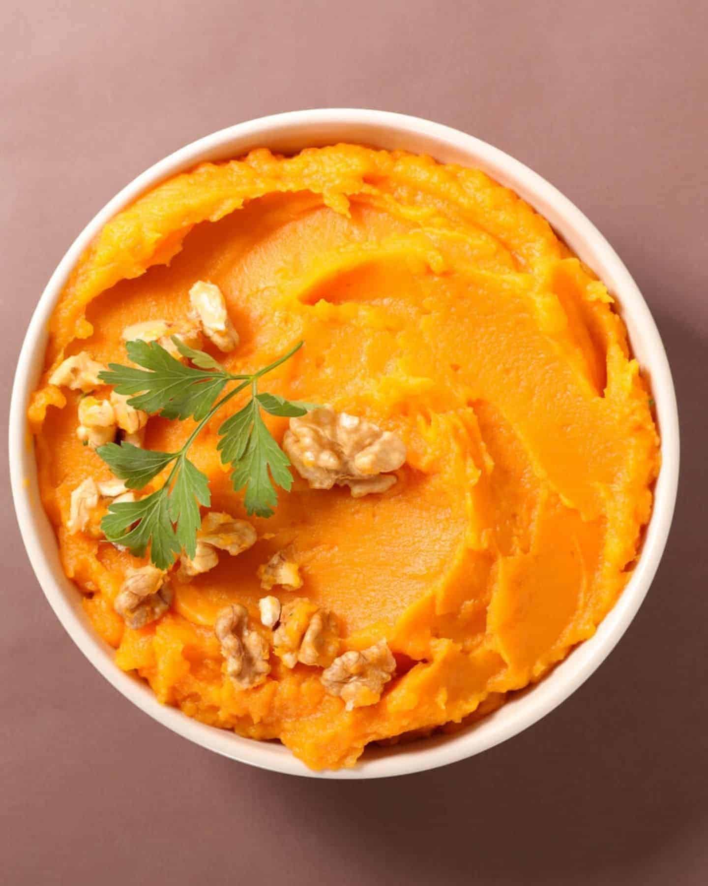Sweet potato mash in a white bowl  with herbs and nuts on top