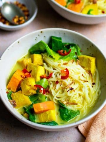 A bowl of vegan khao soi. It's filled with noodles, sweet potato, greens and tofu.