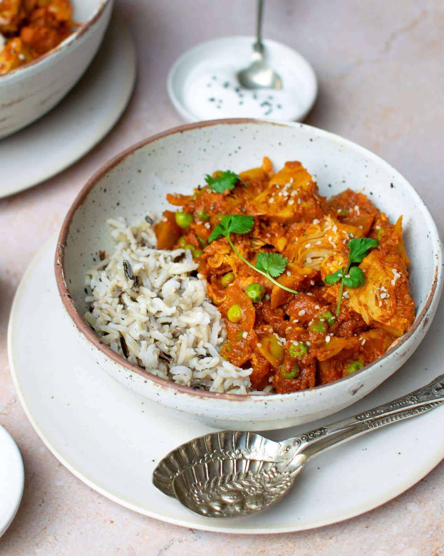 Curry and rice in a bowl with yoghurt behind in a small pot, as a serving suggestion