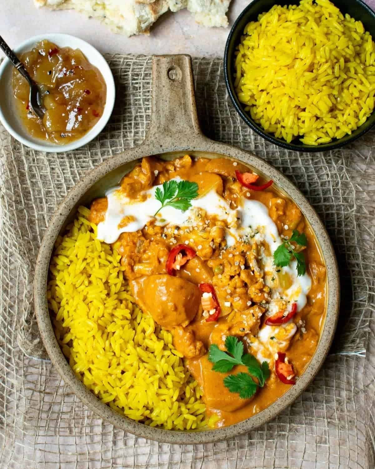 Veggie tikka masala top down view with vegan yoghurt on top, served with pilau rice, chutney and naan bread.