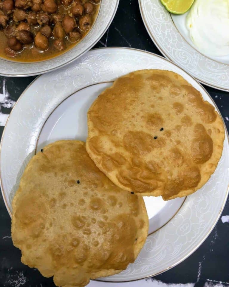 A top down view of some deep fried Indian bread with two plates in the top two corners that are visible