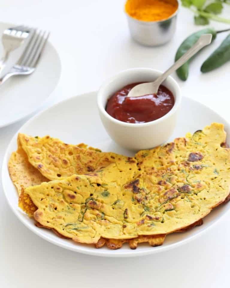 A white plate of chickpea flatbreads with a pot of ketchup next to it with a spoon in it