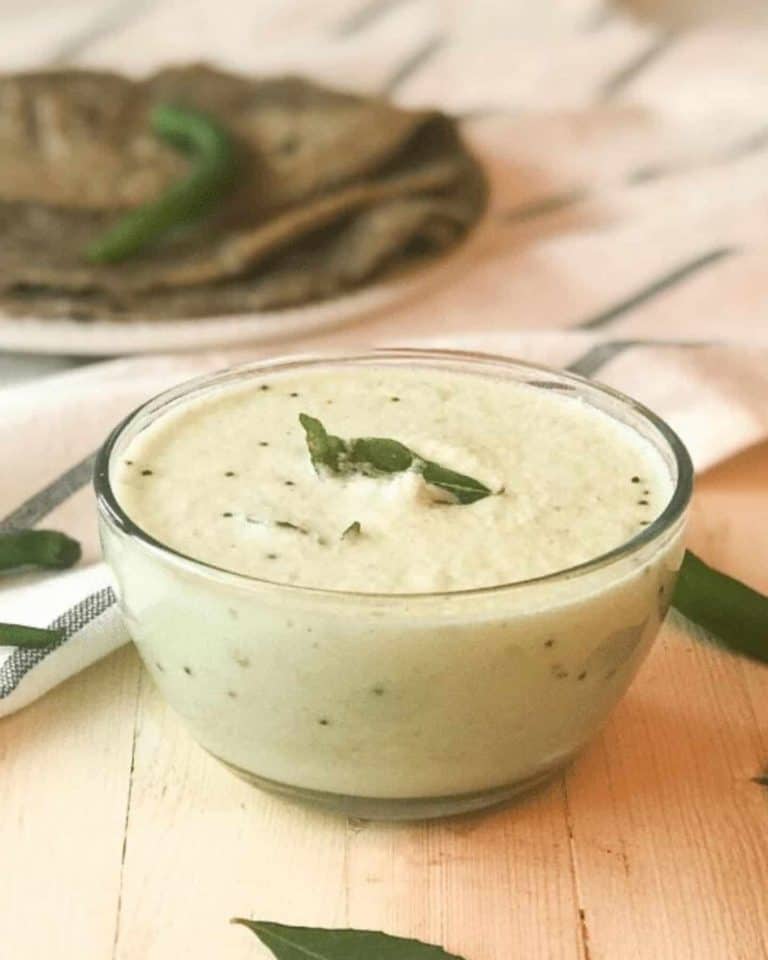 A glass bowl full of white coconut chutney with bay leaves on top of it