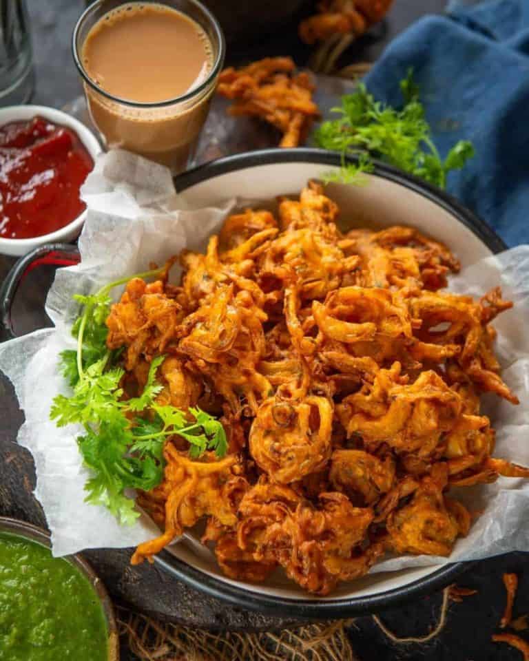 A plate full of onion pakodas with condiments around it like green chutney, chai tea and ketchup