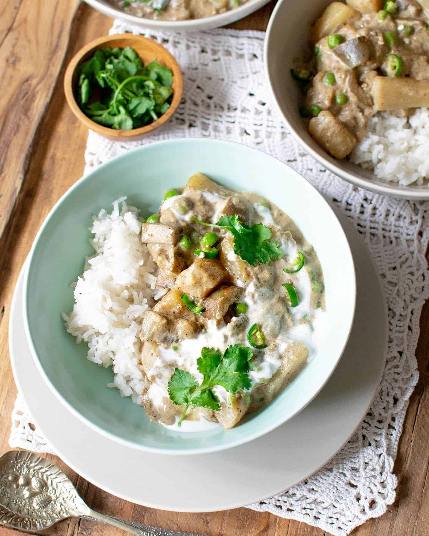 Top down view of vegan korma in a green bowl with fresh coriander in a bowl behind it and another bowl just poking into the frame in the top right