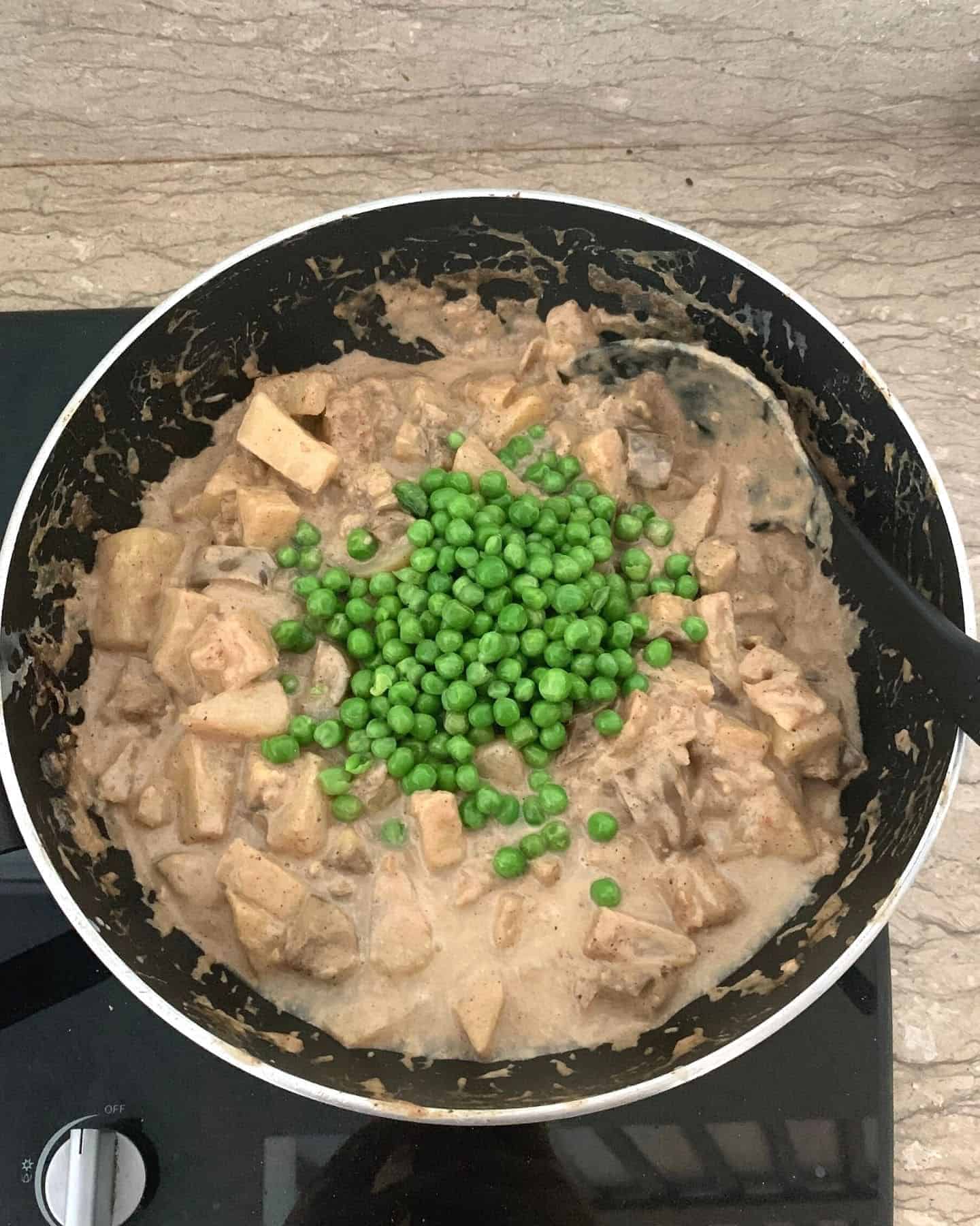 Peas on top of a brown curry in a pan on a hob