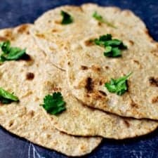 Close up of vegan roti laid out on top of each other with coriander on top, all on a dark blue background