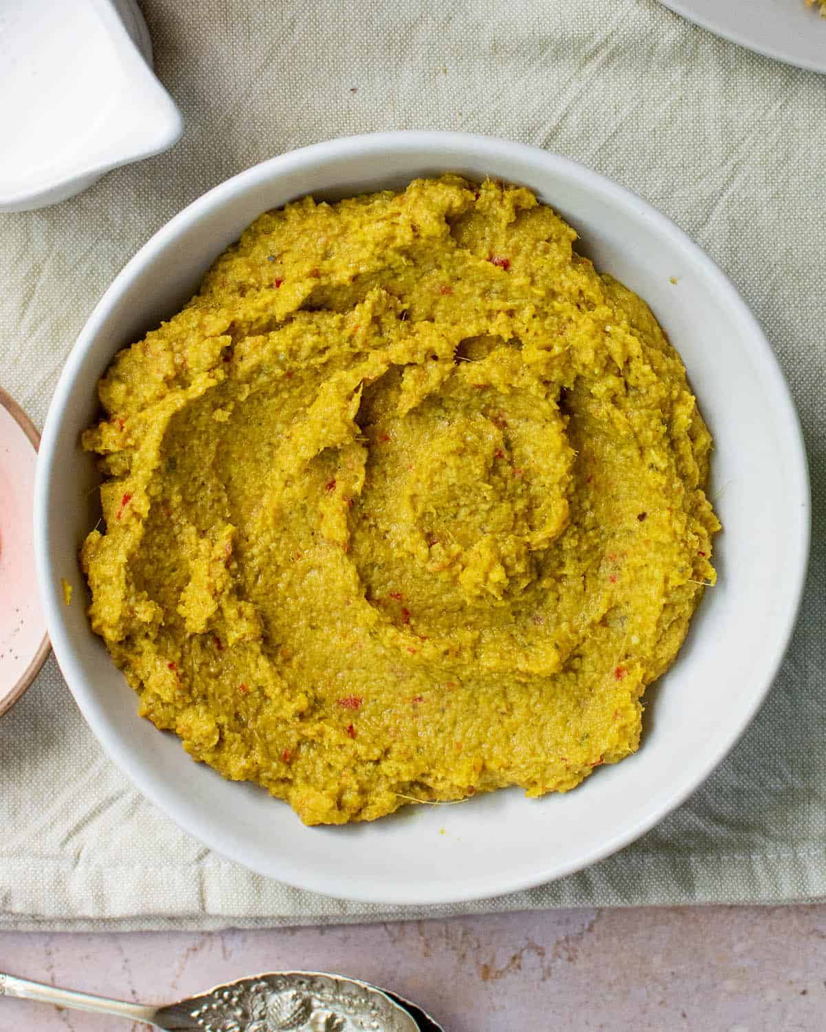 Close up of a yellow curry paste in a white bowl on a cream cloth