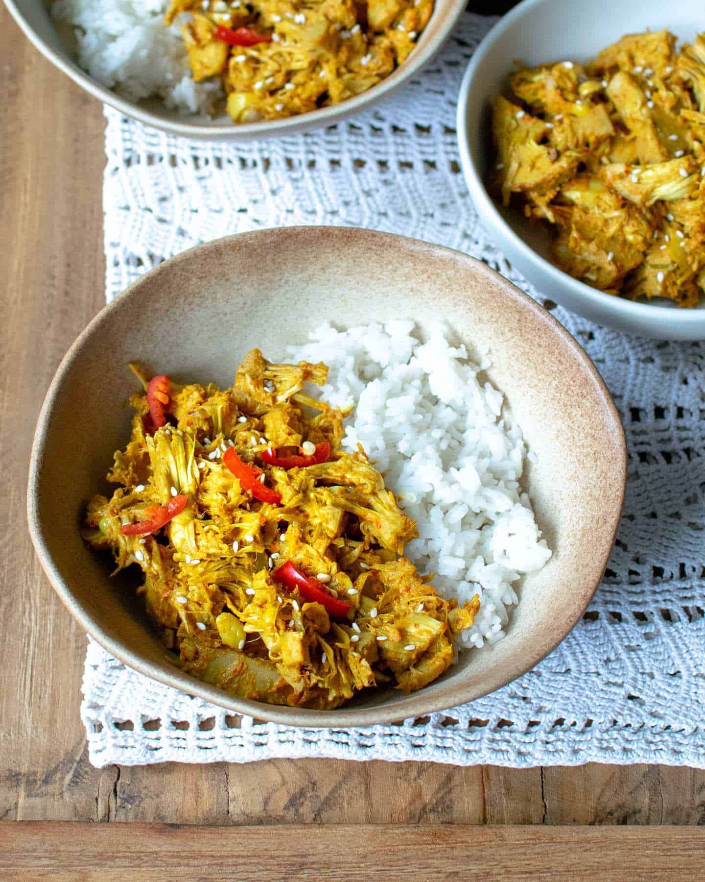 Top down view of jackfruit rendang in alight brown bowl with 2 more bowls around it also showing the curry