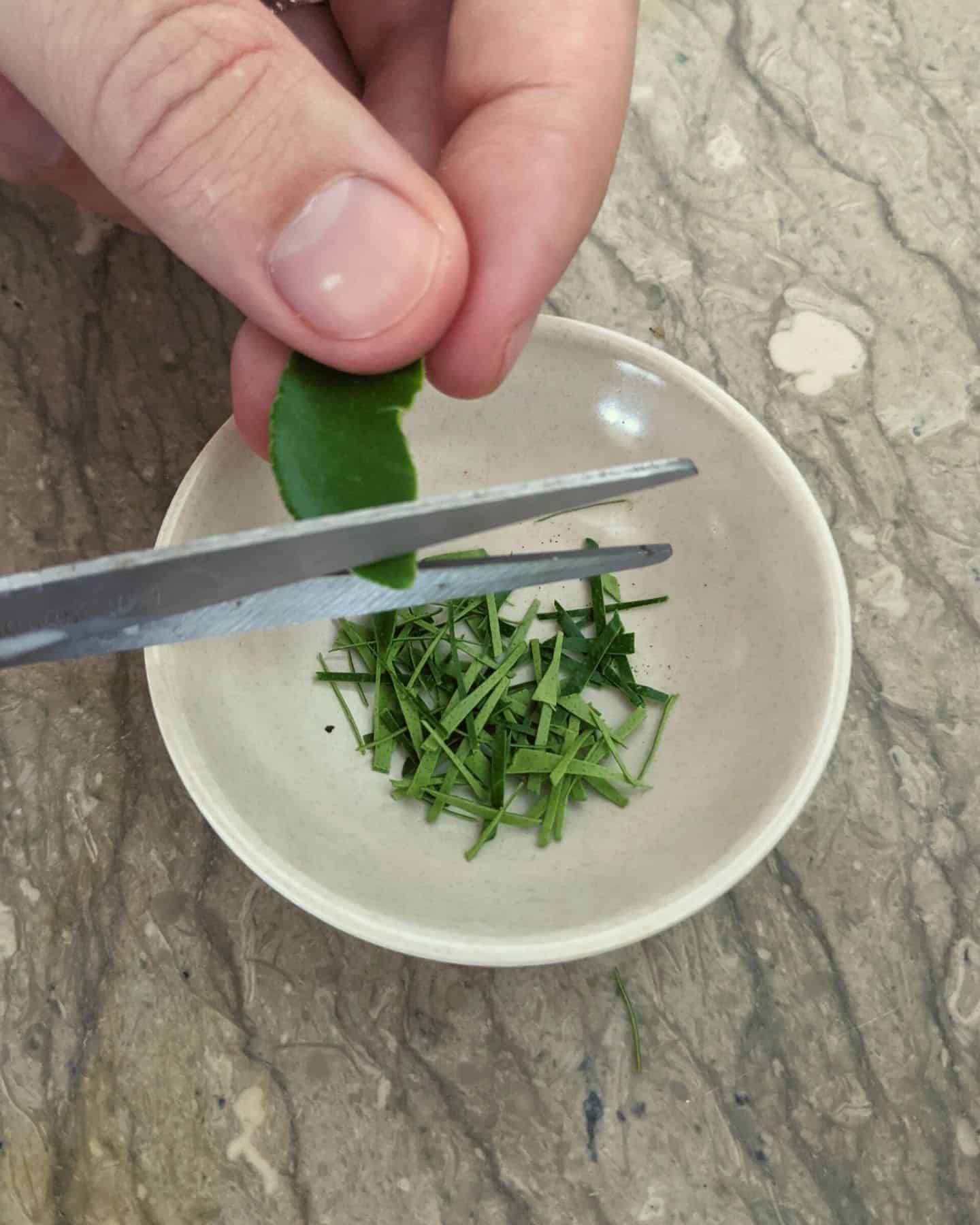 A kaffir lime leaf being chopped with scissors over a small dish