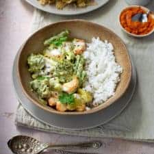 Square image of Balinese vegetable curry in a brown bowl with sambal in the background