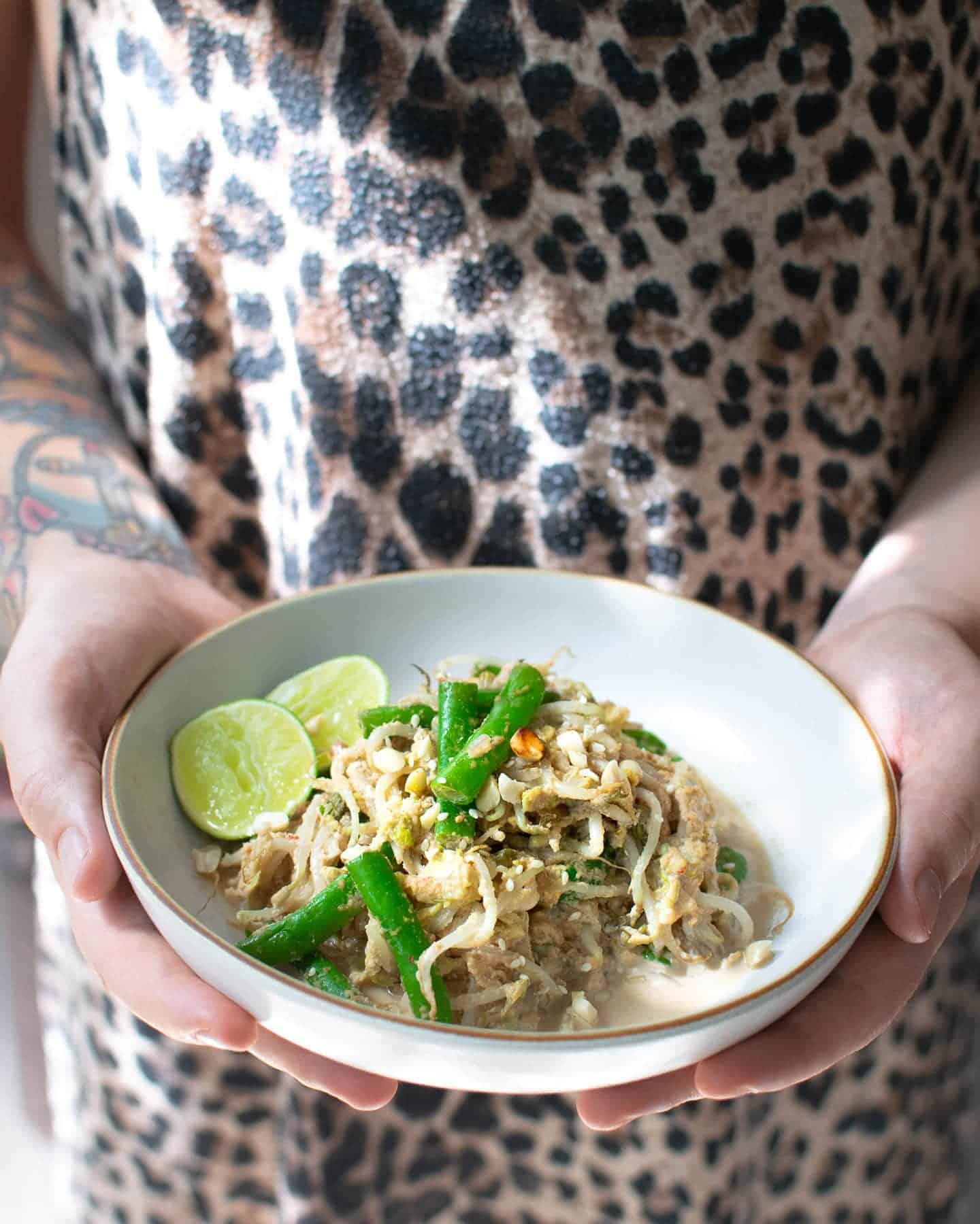 Dan holding a white bowl of vegan gado gado up against his leopard print  top, there's a streak of sunlight shining on his top above the bowl