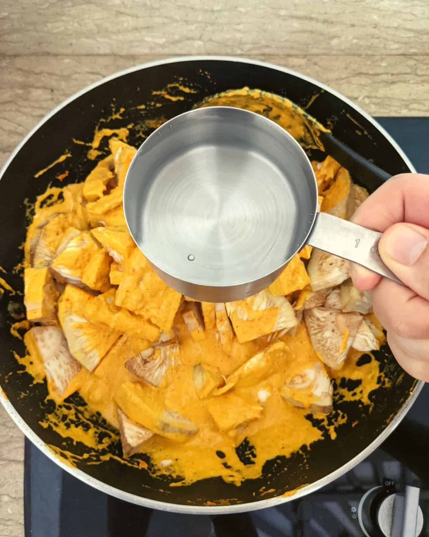 A cup of water being held over a wok with jackfruit in it