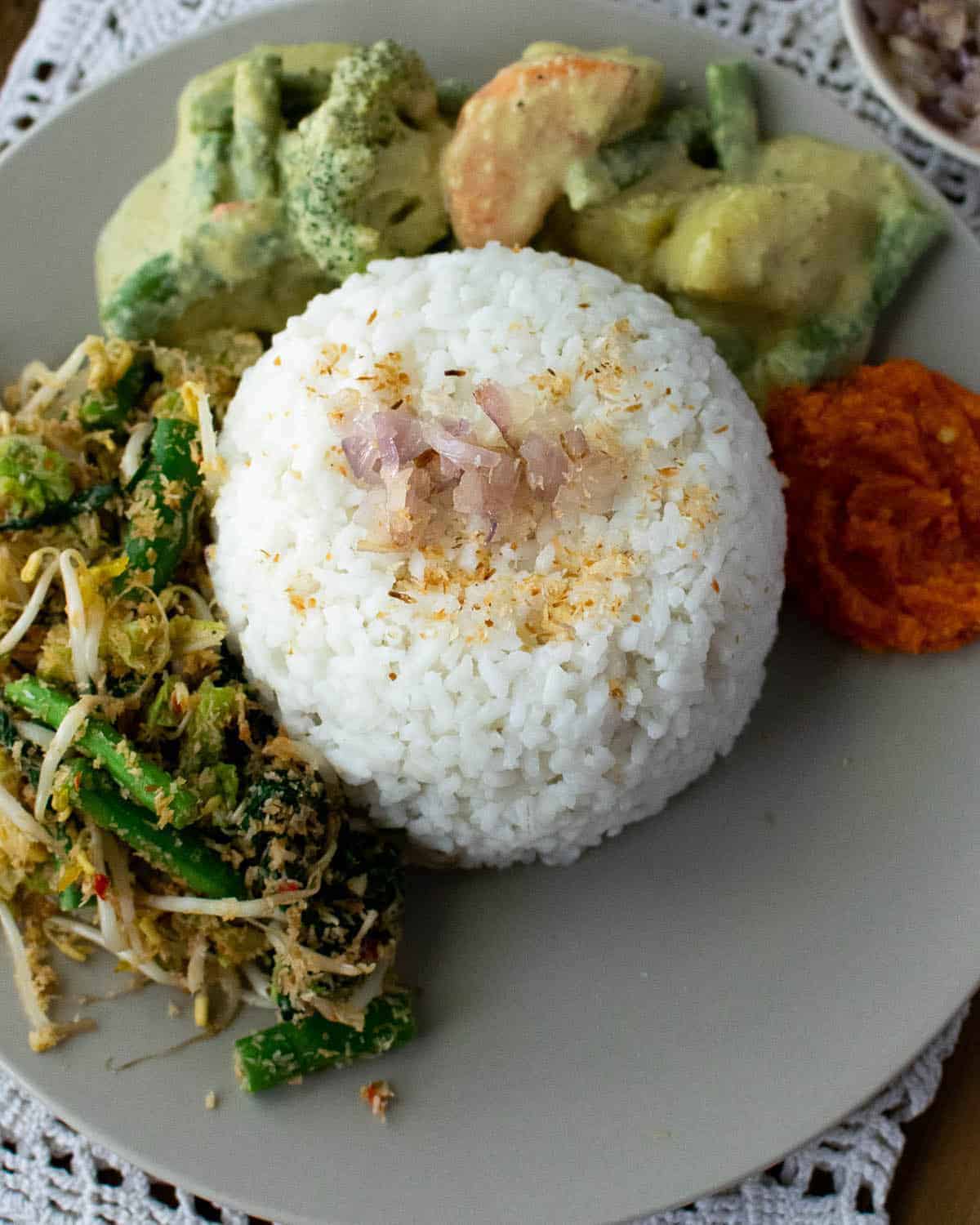 Close up of a dome of nasi uduk (coconut rice) with other vegetable dishes around it