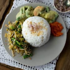 Top down view of nasi uduk in a dome shape with vegetables and sauce around it in an arc