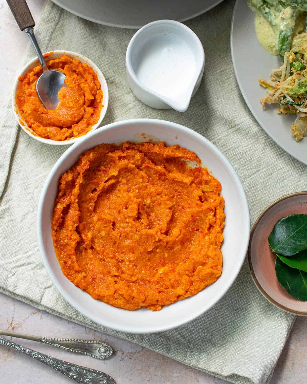 Vegan sambal in a white pot in the centre with additional plates and spoons surrounding it