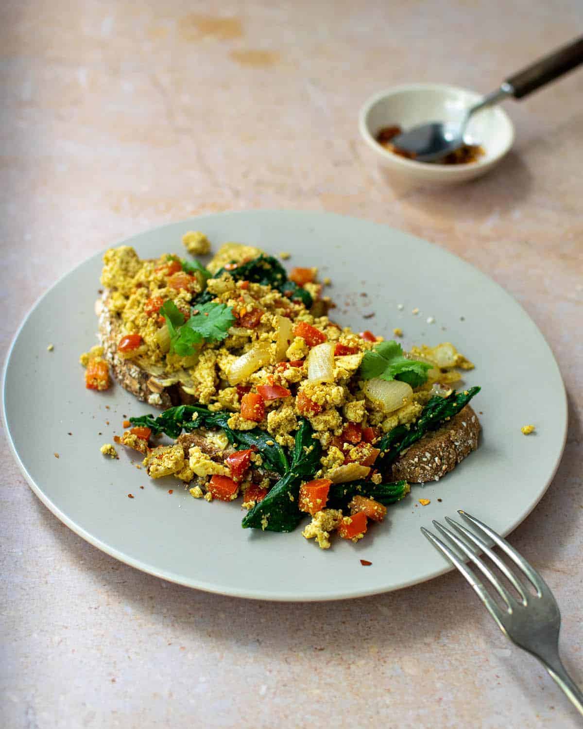 Curry tofu scramble on a piece of toast with a fork perched on the plate