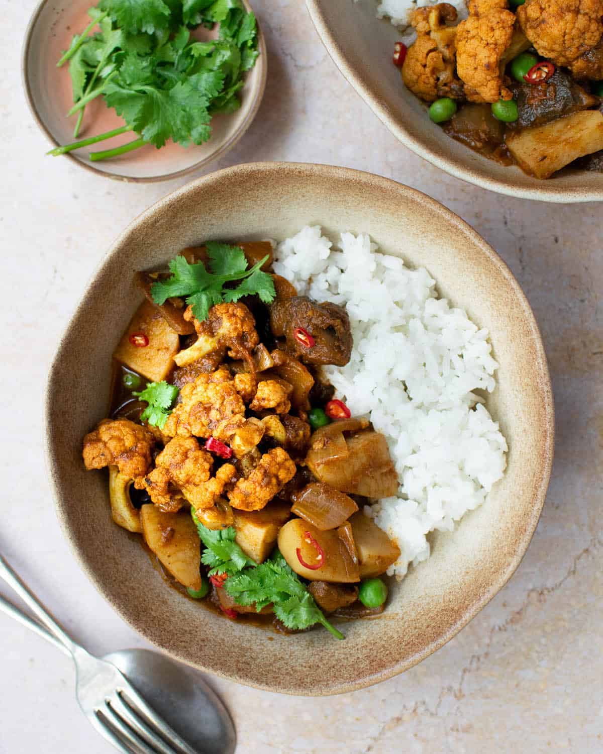 Top down view of vegetable rogan josh in a bowl with rice, with other bowls surrounding it