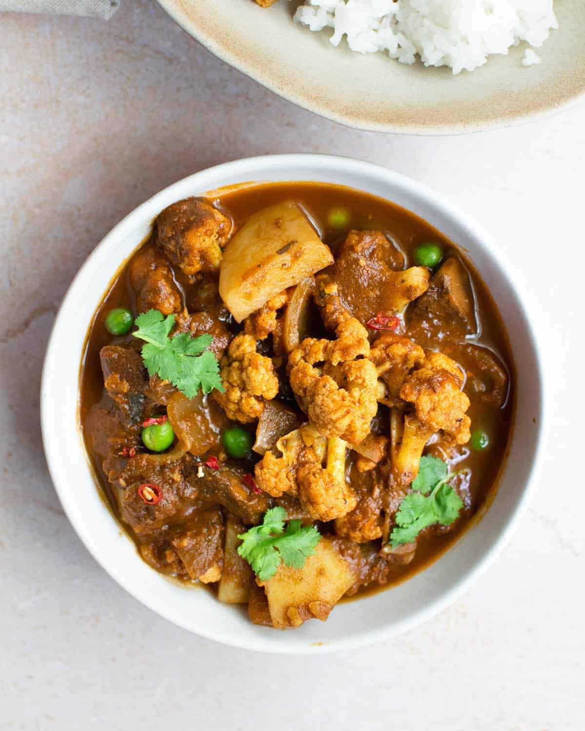 A bowl full of vegetable rogan josh with cauliflower, peas and potato