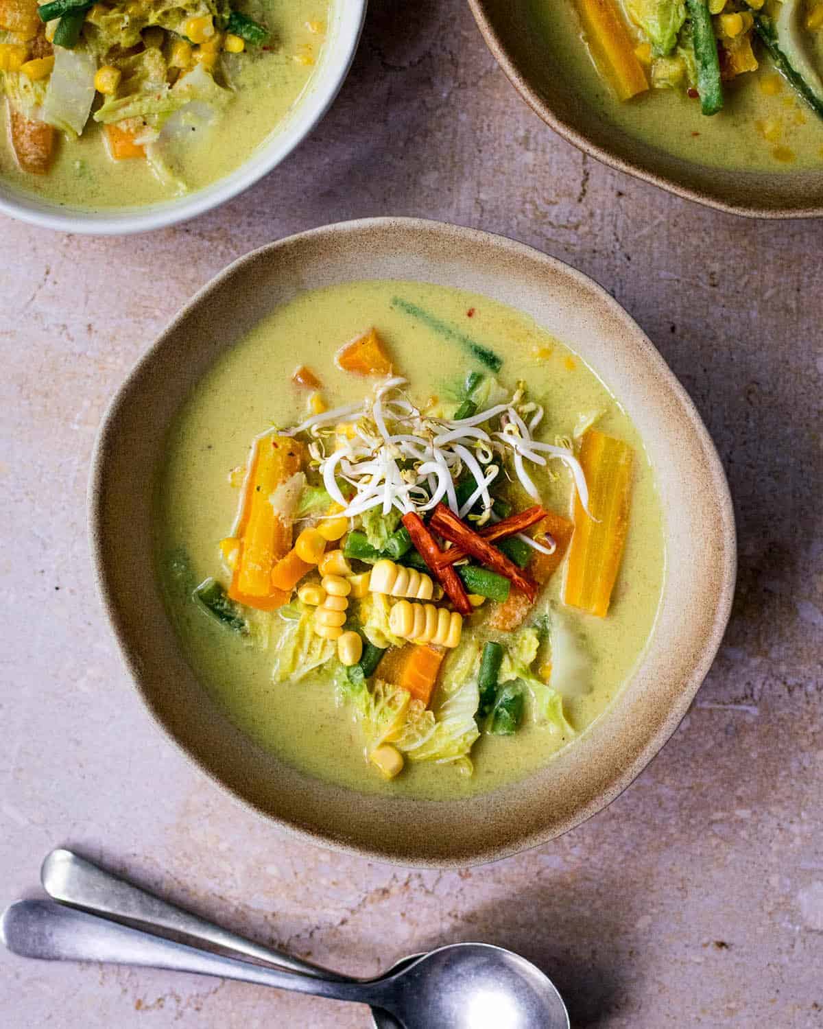 Sayur lodeh (vegetables in coconut milk) in a bowl with two spoons in front of it and bowls in the background