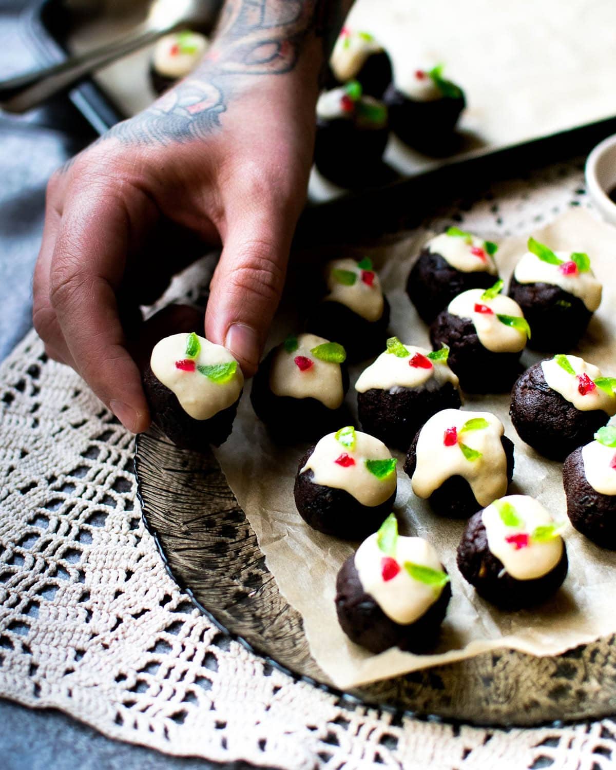 A plate of vegan mini chocolate Christmas puddings with a hand holding one up