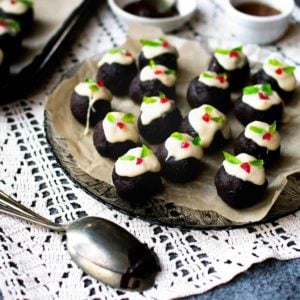 Mini chocolate Christmas puddings on a glass plate with a tray to the left of them