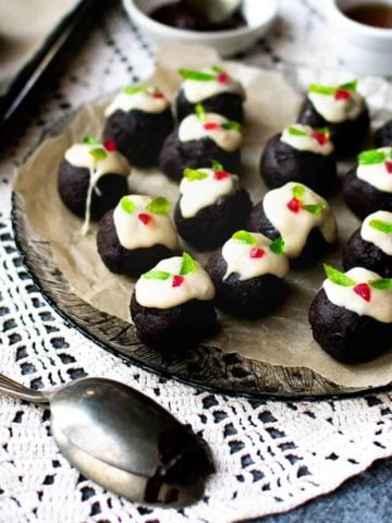 Mini chocolate Christmas puddings on a glass plate with a tray to the left of them