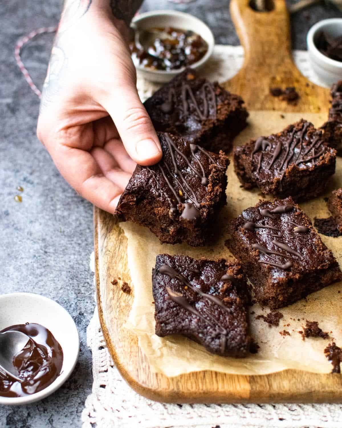 5 vegan Christmas brownies on a board with a hand about to pick one up