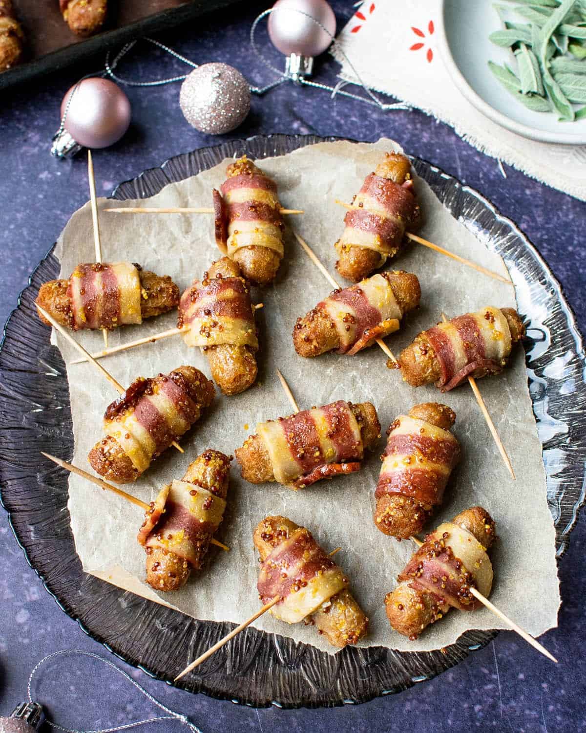 Vegan pigs in blankets on a plate with sage in the background