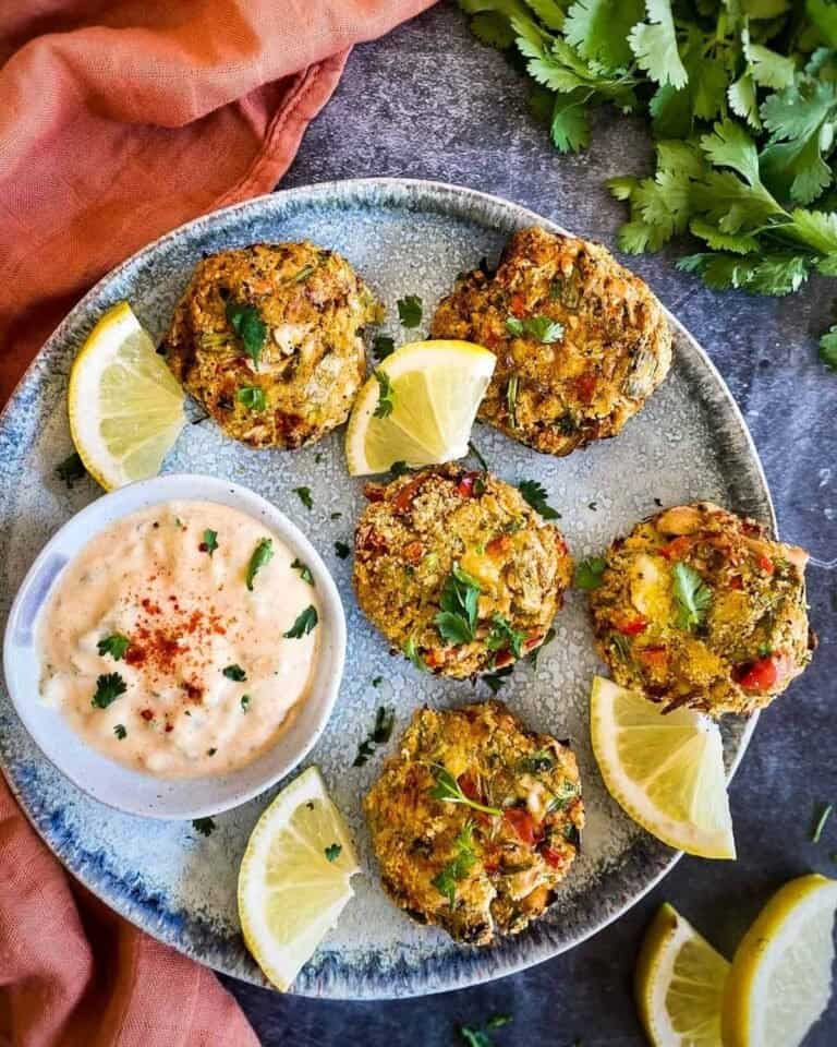 Vegan crab cakes on a blue plate with a dip in a pot.