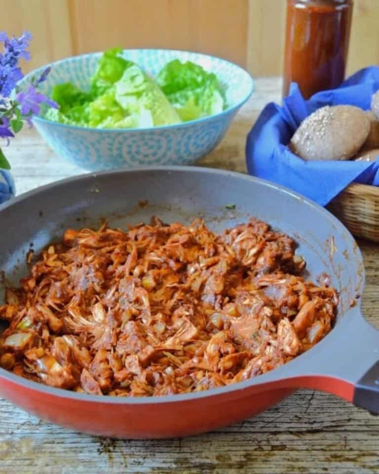 Pulled jackfruit with sauce in pan, lettuce in a bowl in the background.