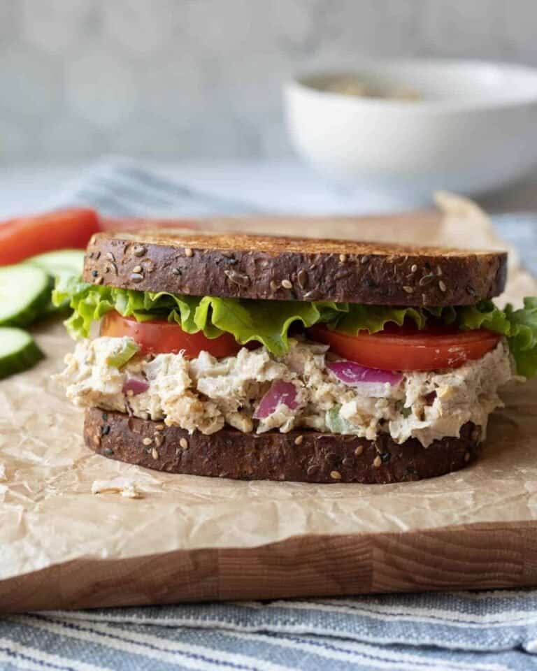 Vegan chicken salad sandwich on brown bread served on a wooden chopping board.