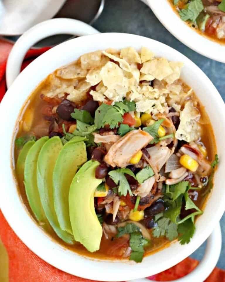 Vegan taco soup in a white bowl with handles topped with avocado.